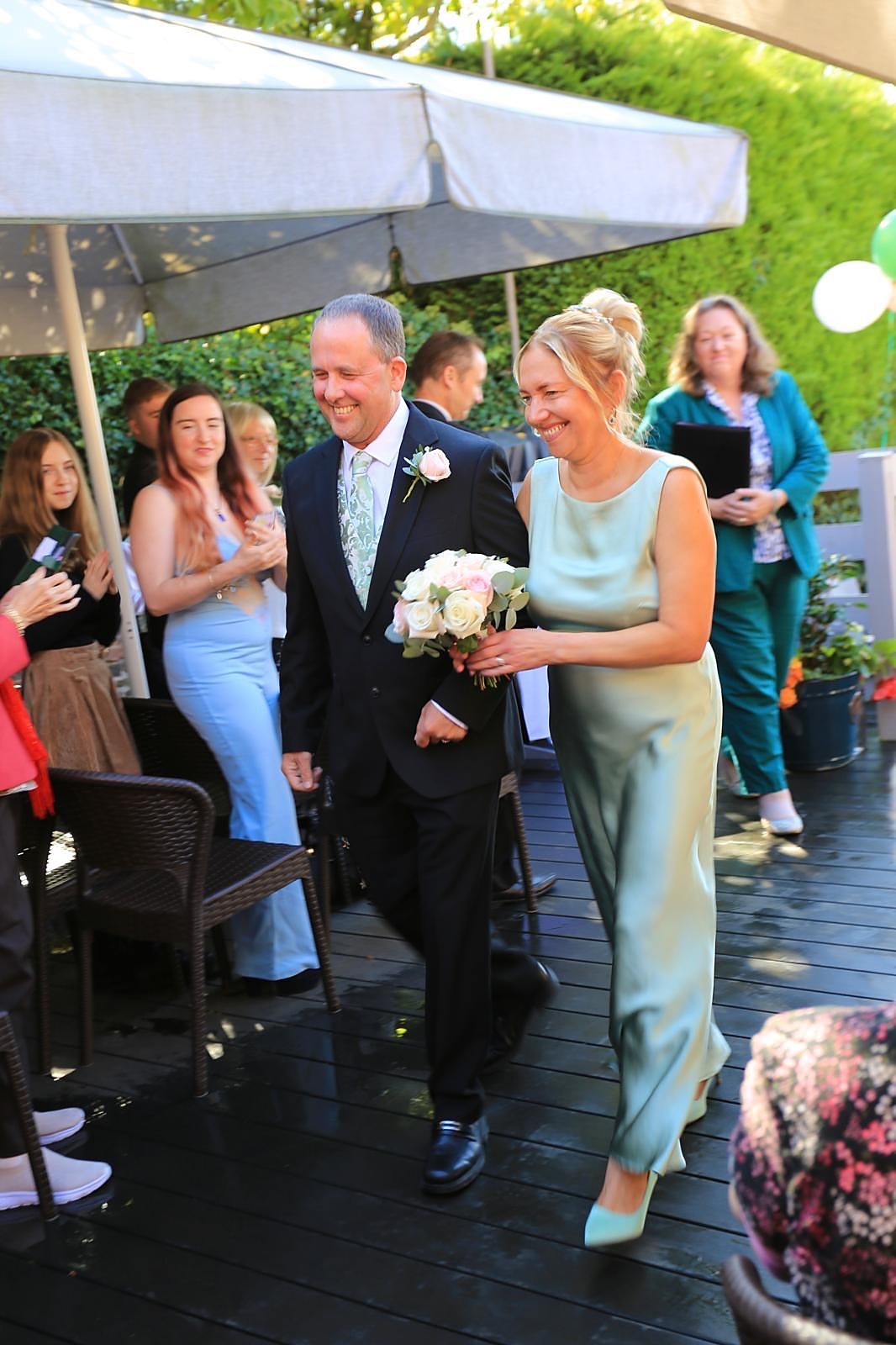 Debbie and Barry walking down the aisle together as guests applaud at The Old Red Lion in Milton Keynes